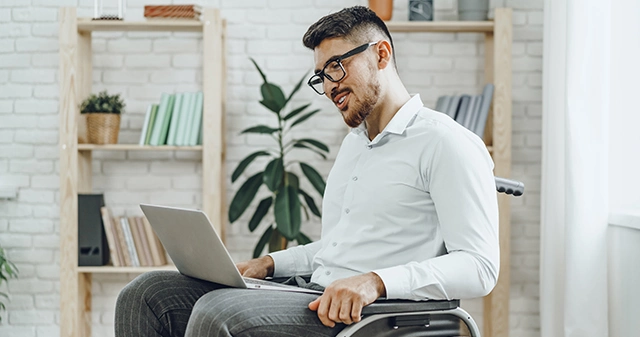 Młody mężczyzna na wózku inwalidzkim pracuje na laptopie w jasnym biurze, symbolizując cyfrową dostępność i inkluzywny design.